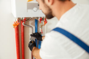 Closeup of plumber working with water pipes while installing heating system in apartment, Clogged Drain Repair Bloomington IL