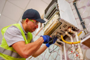 A technician in a green vest and hat carefully works on the internal components of a wall-mounted boiler, ensuring hot water supply for home comfort and efficiency, Tankless Water Heaters Bloomington IL